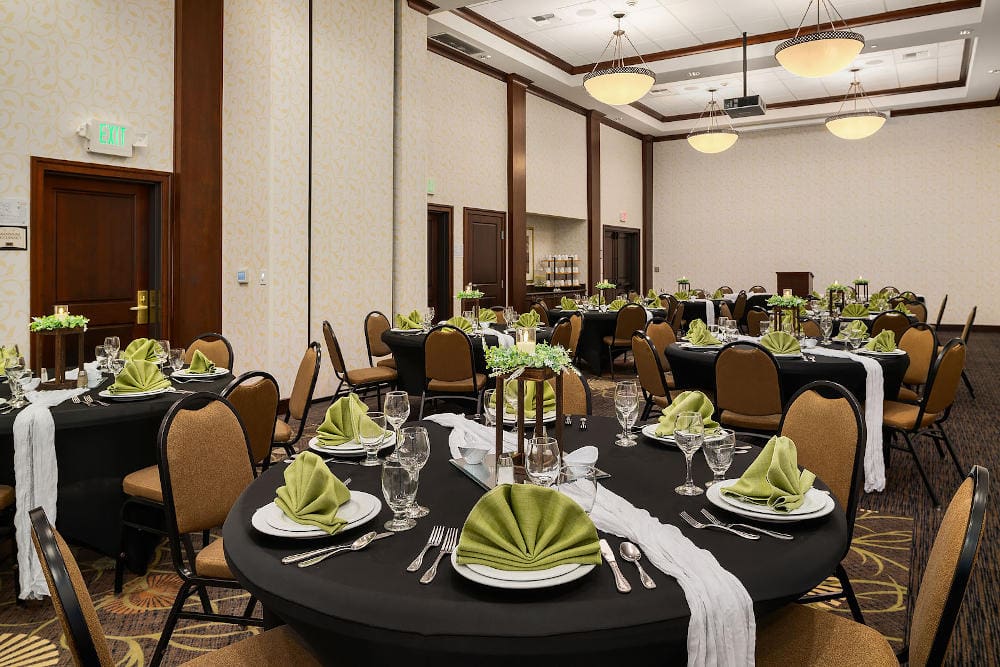 ballroom with circular tables throughout topped with plates baring decorative green napkins